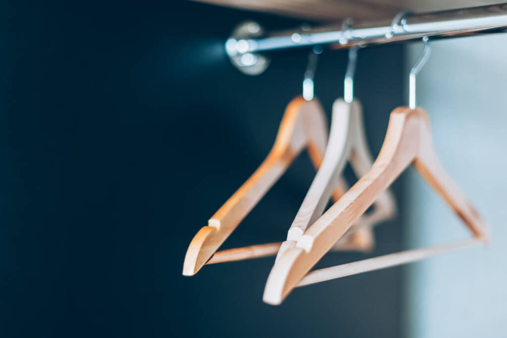 Empty Wooden hangers on rail in closet. Lifestyle composition with natural light and copy space